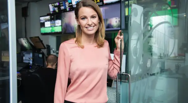 Jennie Pierrou ler vid en glasdörr i en kontrollrumsmiljö med många skärmar.