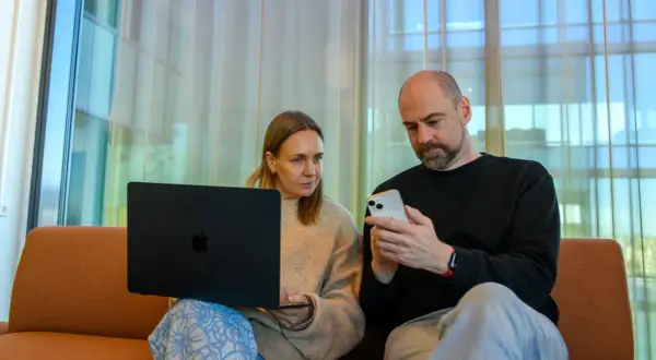 Man och kvinna sitter i soffa med laptop och mobil. De verkar diskutera något från samtiden tidning.