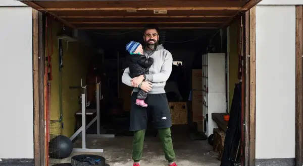 Man holding a baby in a garage with gym equipment.