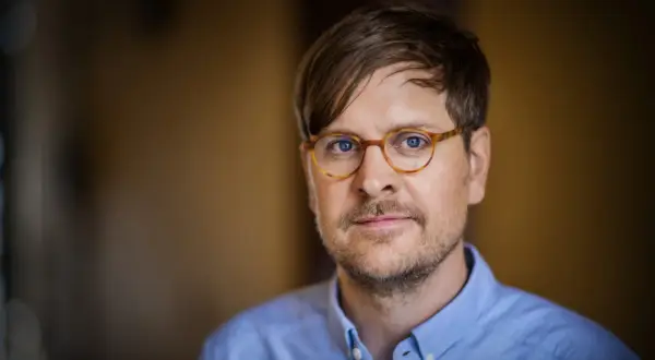Sune Kempe, en man med glasögon och blå skjorta, tittar in i kameran.