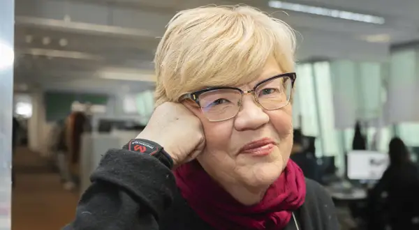 Lena Mellin med glasögon och en vinröd scarf vilar huvudet i handen.