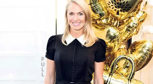 Andrea Brodin, klädd i svart med vit krage, ler vid ett firande med glänsande guldfärgade ballonger. Metro Mode.