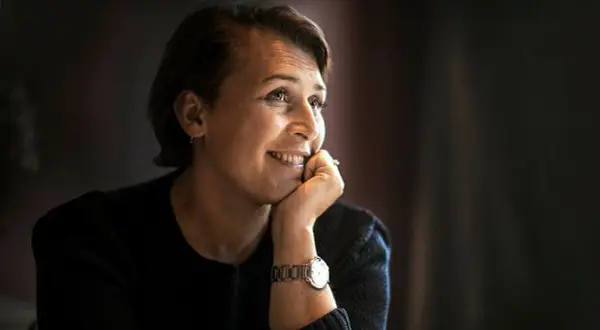 Hanna Widell ler och vilar hakan i handen, klädd i en mörk tröja med en klocka på handleden.