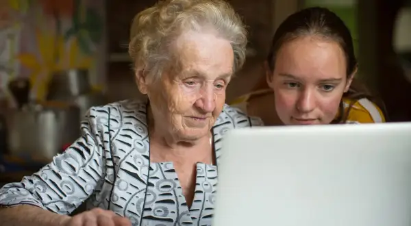 En äldre kvinna och en ung flicka tittar på en laptop. De lär sig om nya medier, en kontrast till traditionella medier.