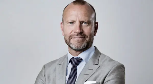 Peter Fellman, en man med gråsprängt skägg och blå ögon, bär en ljusgrå kavaj och randig slips.