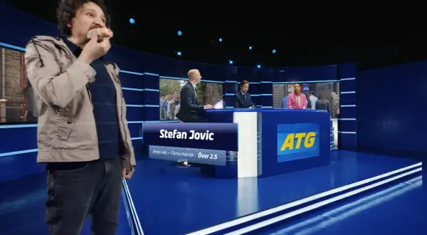 Man äter korv i en studio med ATG-reklam.