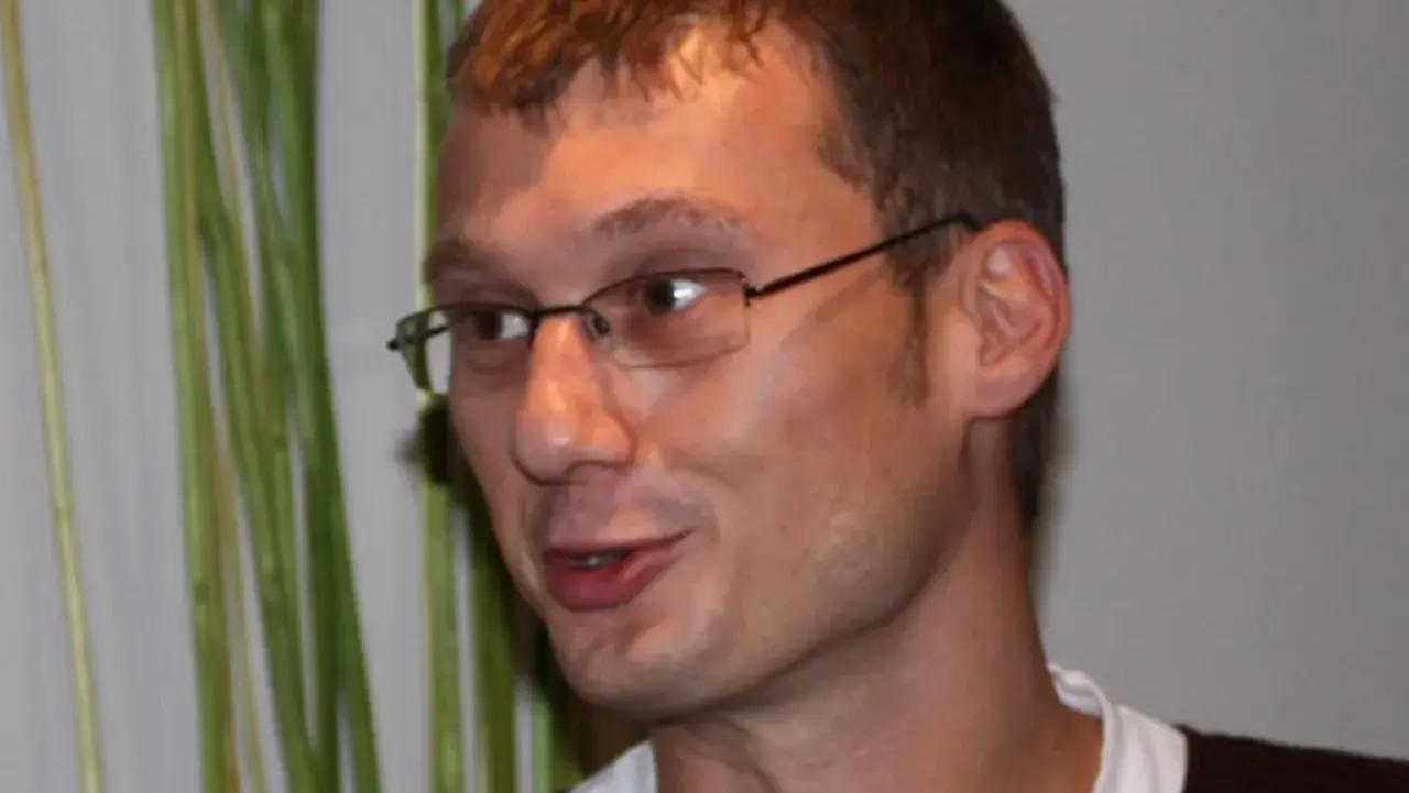 Sladjan Osmanagic, en man med glasögon, ler mot kameran. Bakom honom syns gröna växter.