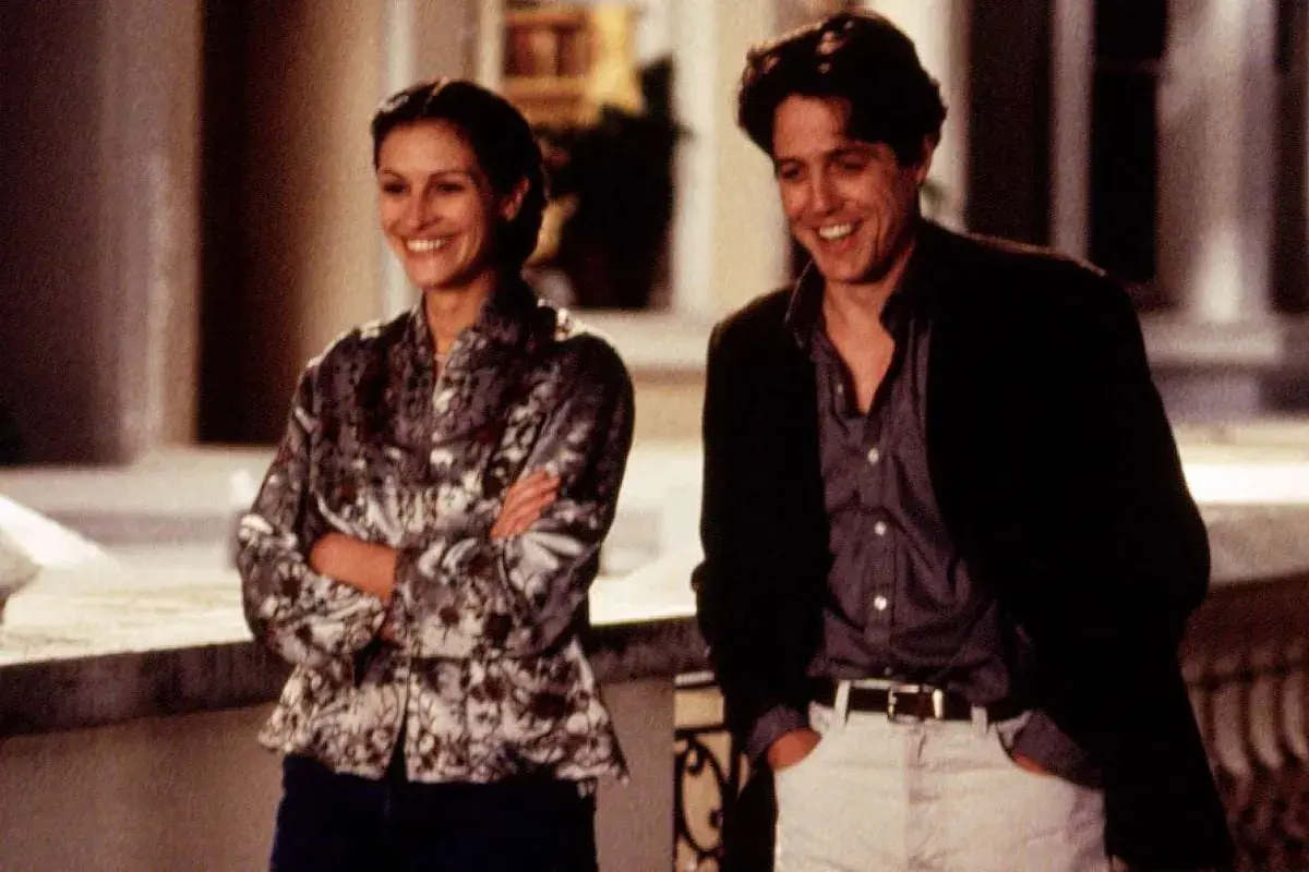 Julia Roberts young och Hugh Grant skrattar tillsammans utomhus.