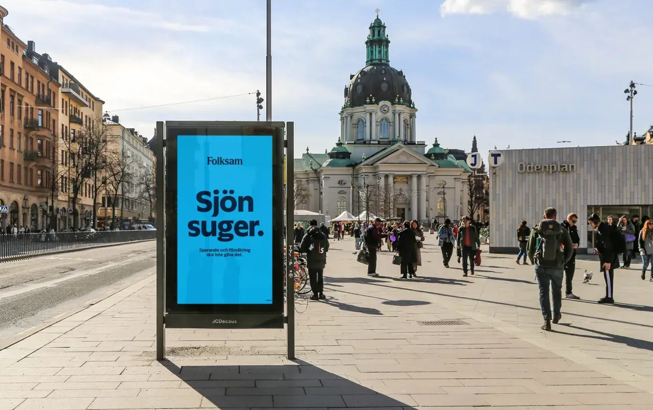 Folksam reklam på en blå skylt i en stadsmiljö. "Sjön suger" står det, med texten "Sparande och försäkring ska inte göra det." under.