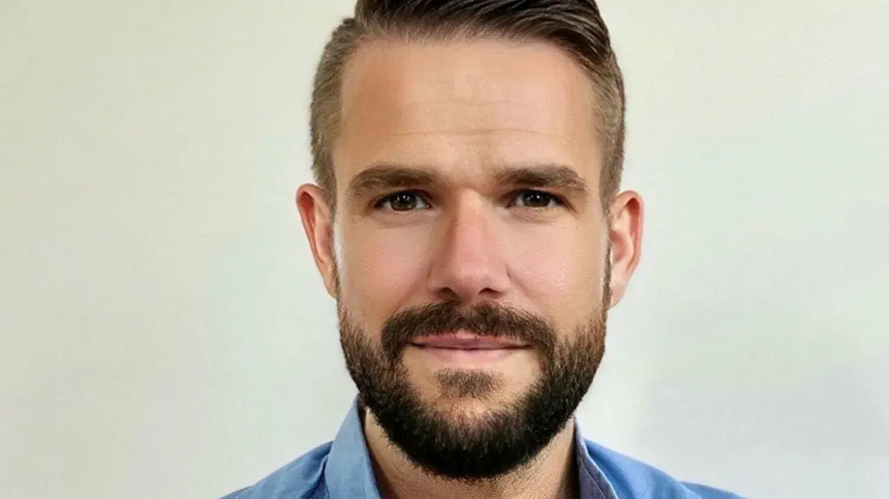 Johnny Kroneld, en man med kortklippt mörkt hår och skägg, bär en blå skjorta.