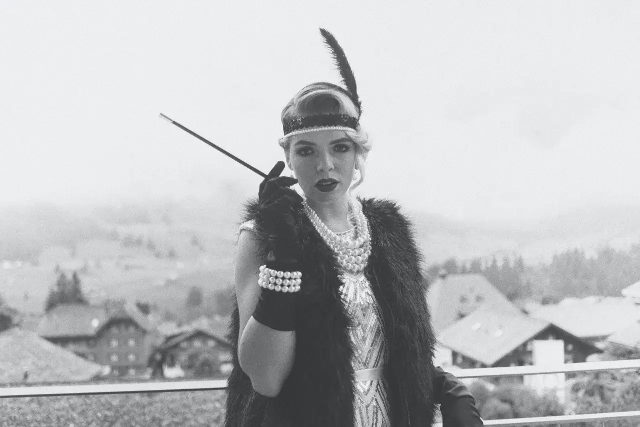 Kvinna i 1920-talsmode med fjäderpannband, pärlhalsband och cigaretthållare.