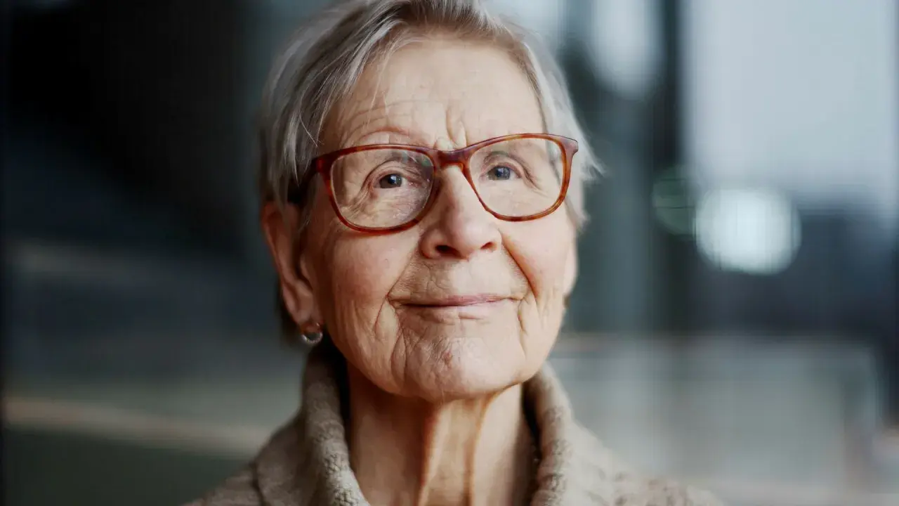 Kerstin Brunnberg, en äldre kvinna med glasögon och grått hår, ler mjukt.