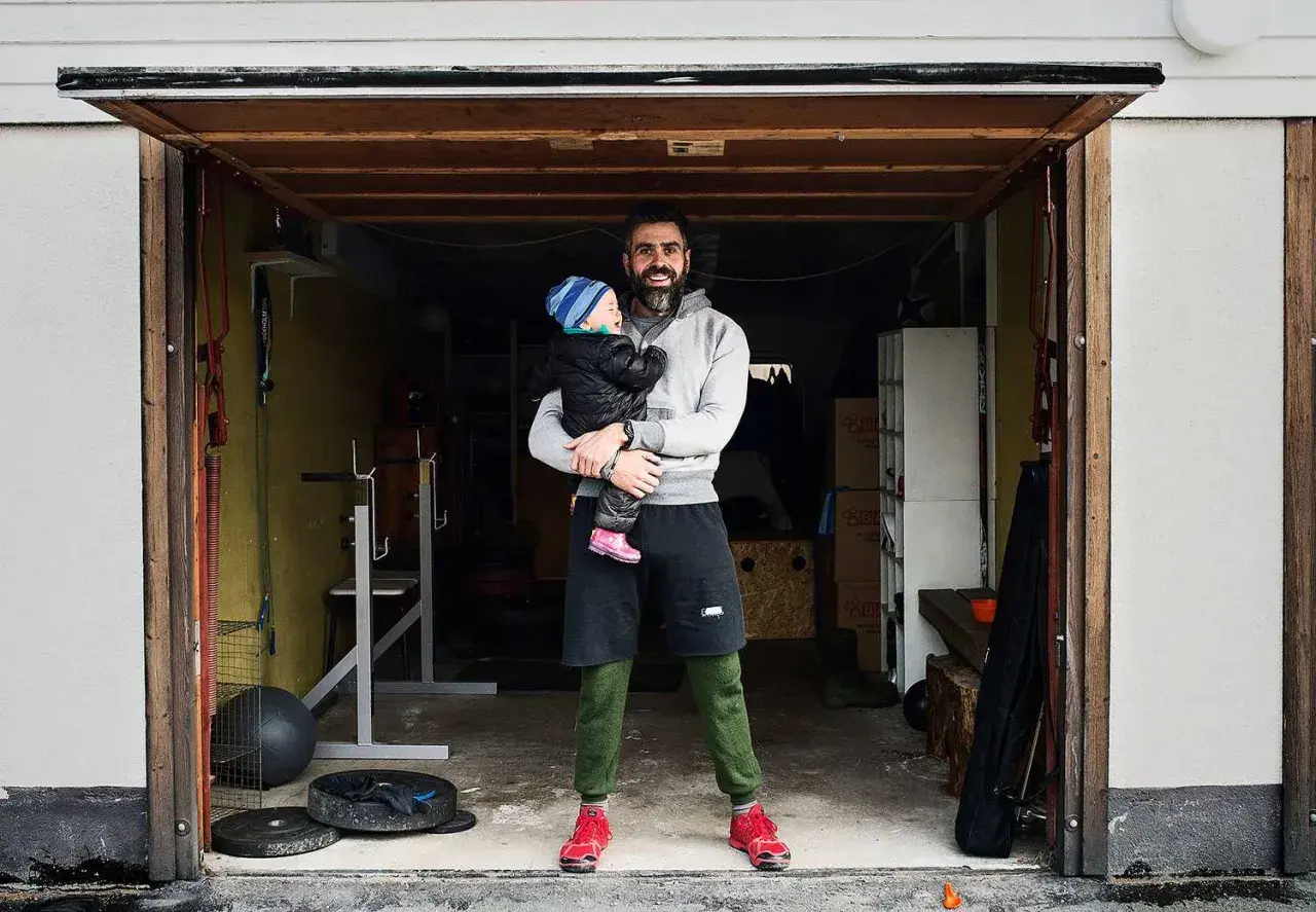 Man holding a baby in a garage with gym equipment.