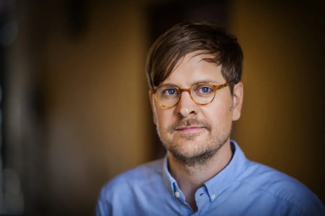 Sune Kempe, en man med glasögon och blå skjorta, tittar in i kameran.
