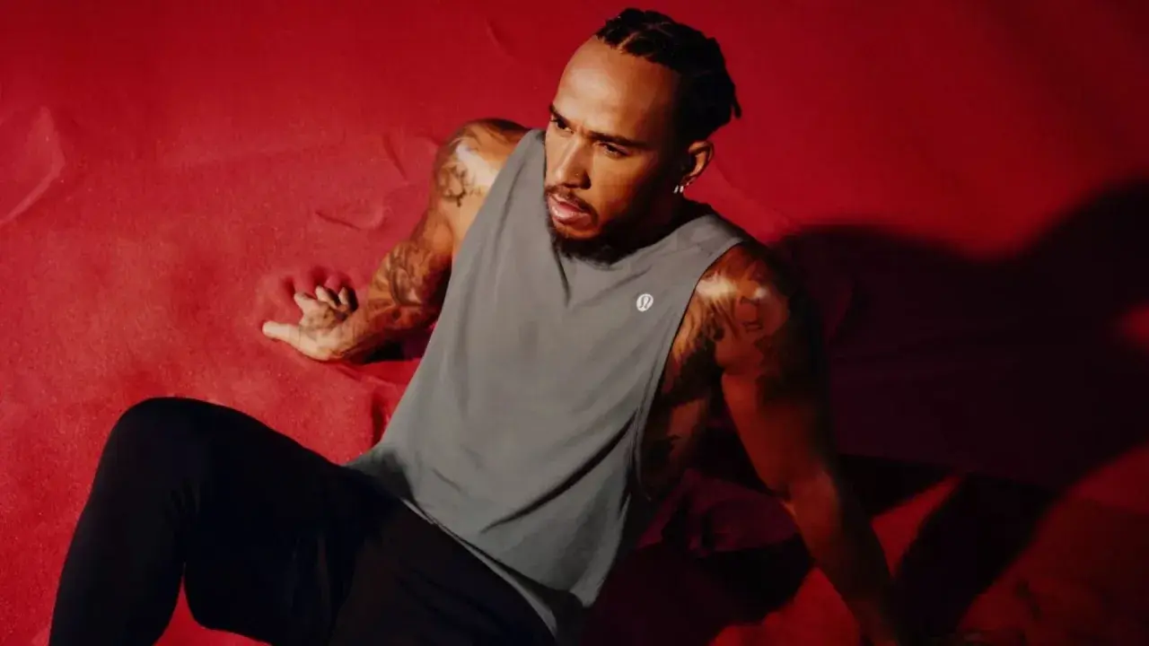 Lewis Hamilton visar upp sin Lewis Hamilton fashion-stil i en grå linne och svarta byxor, sittandes på en röd yta.