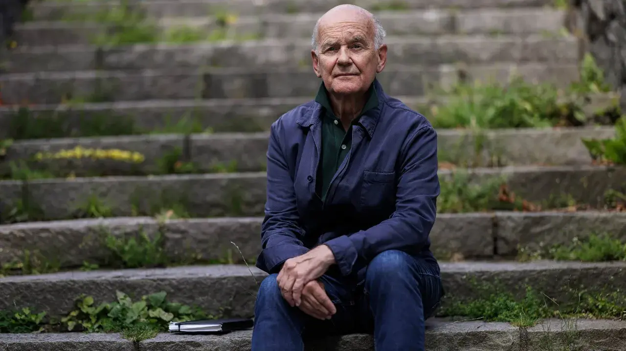 Johan af Donner sitter på en trappa utomhus, klädd i en mörkblå jacka och jeans. En anteckningsbok ligger bredvid honom.