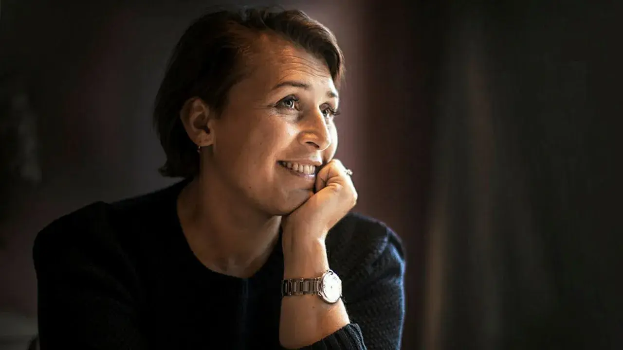 Hanna Widell ler och vilar hakan i handen, klädd i en mörk tröja med en klocka på handleden.
