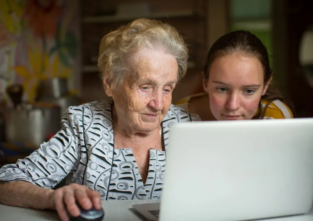 En äldre kvinna och en ung flicka tittar på en laptop. De lär sig om nya medier, en kontrast till traditionella medier.
