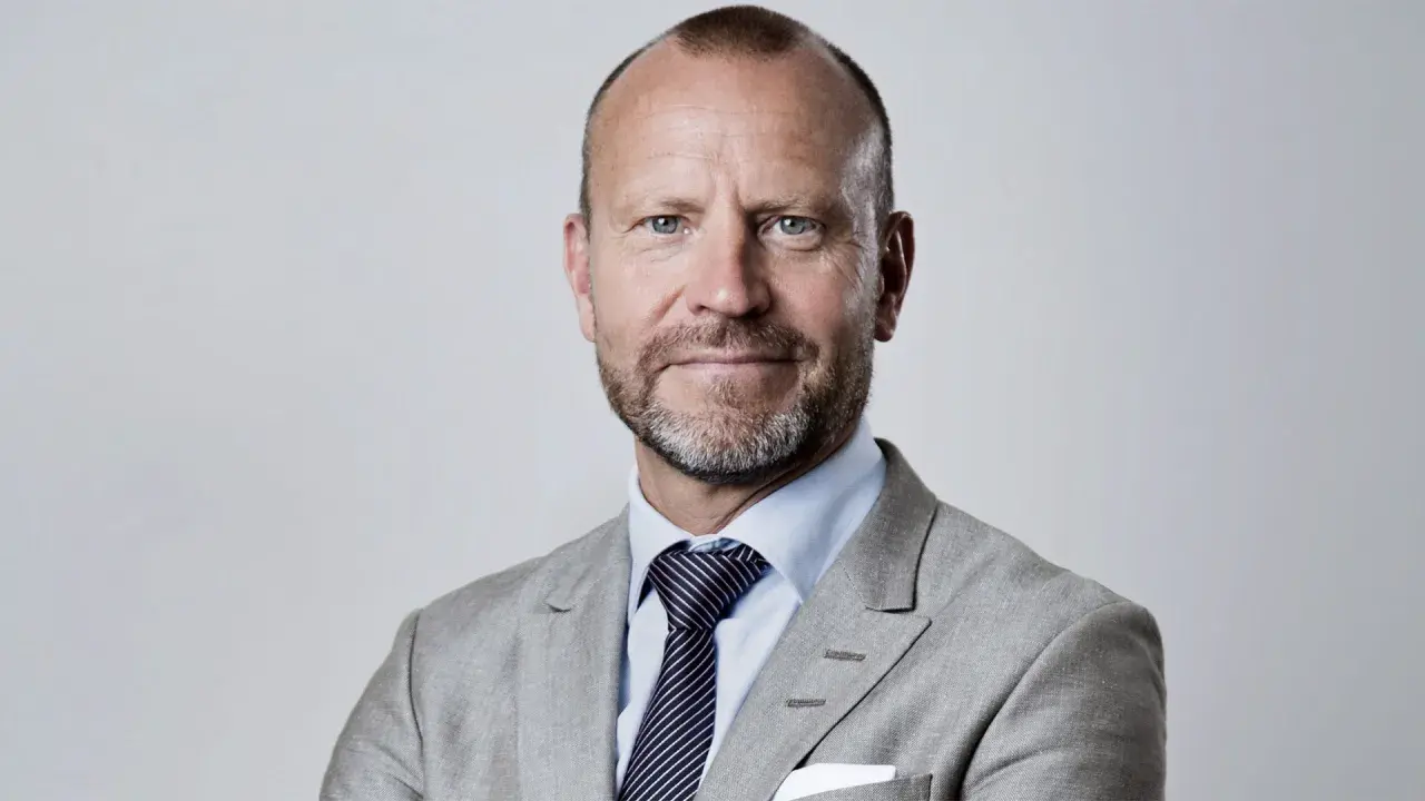 Peter Fellman, en man med gråsprängt skägg och blå ögon, bär en ljusgrå kavaj och randig slips.