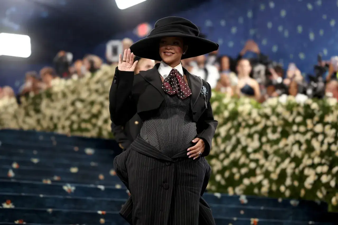 Rihanna, gravid och strålande, vinkar till publiken i en dramatisk svart outfit med hatt.