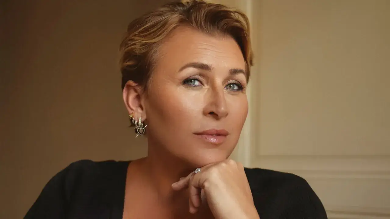 Hanna Widell, med sitt korta blonda hår och blick som möter betraktaren, vilar hakan i handen. Hon bär en svart tröja och smycken som fångar ljuset.