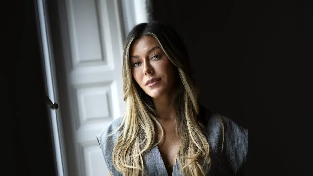 Bianca Ingrosso, med sitt blonda h&aring;r och gr&aring; kl&auml;nning, poserar framf&ouml;r en d&ouml;rr. Kanske v&auml;ntar hon p&aring; sin partner.