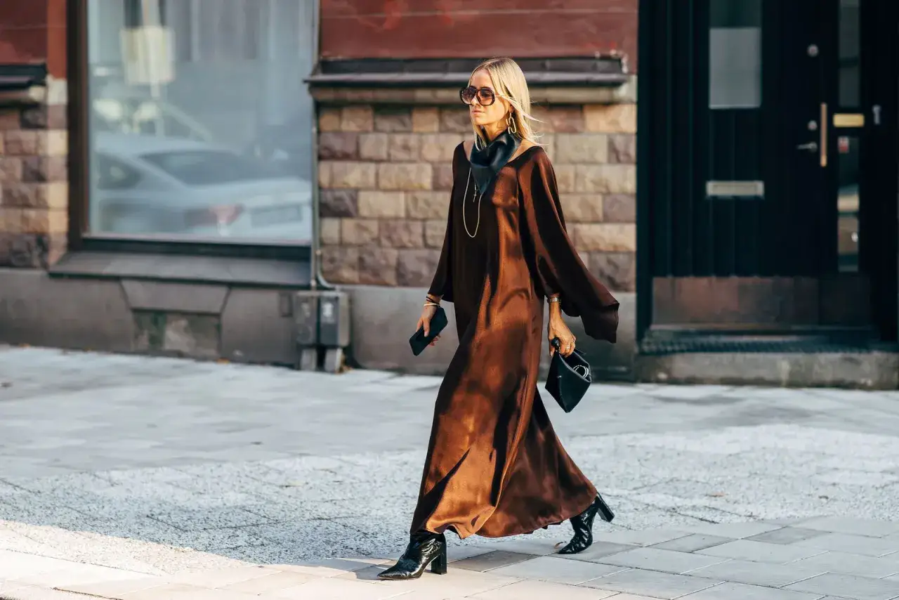 Marie Serneholt i en elegant brun kl&auml;nning och svarta st&ouml;vlar, p&aring; v&auml;g l&auml;ngs en stadsgata.
