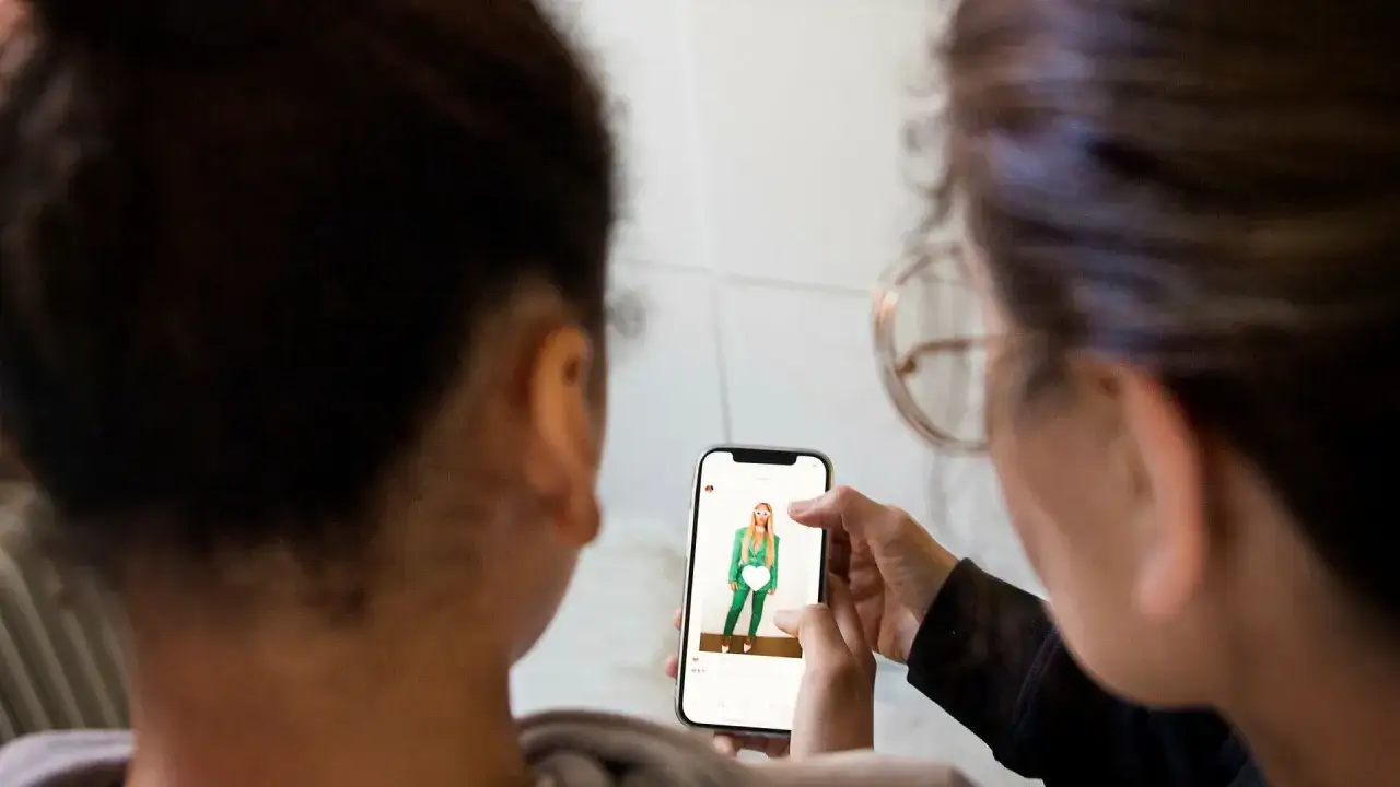 Två personer tittar på en mobilskärm där en person i grön kostym visas. En ny vinkel på alternativ media.