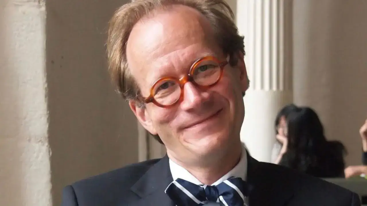 Johan Hakelius, med runda glasögon och fluga, ler mot kameran.