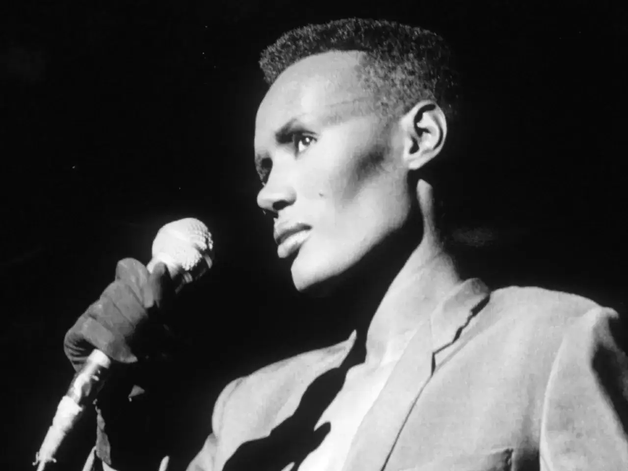 Grace Jones, ikonisk artist, sjunger med mikrofonen i handen. Hennes stil är tidlös, precis som grace jones idag.