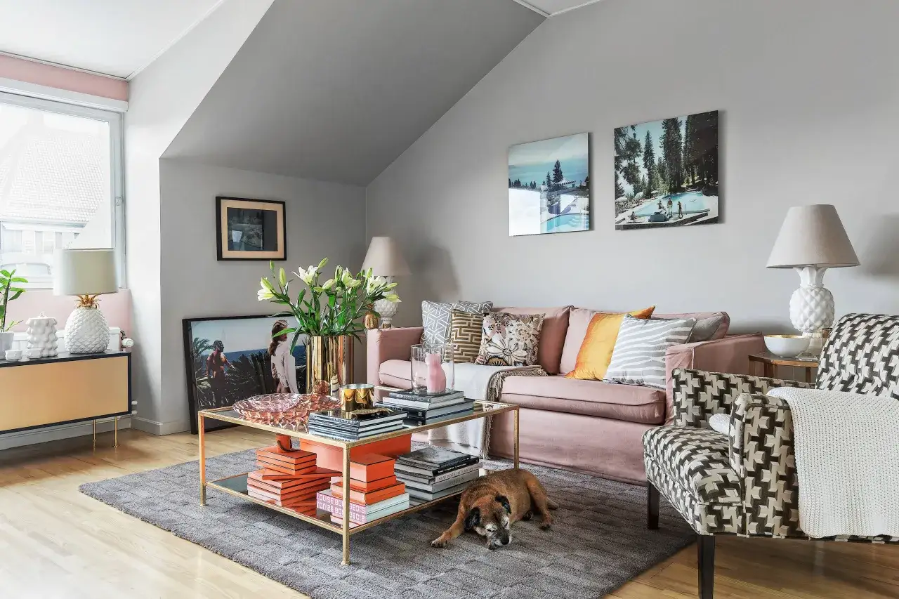Andrea Brodin Metro Mode: Vardagsrum med rosa soffa, mönstrad fåtölj, guldigt soffbord med böcker och en hund som vilar.