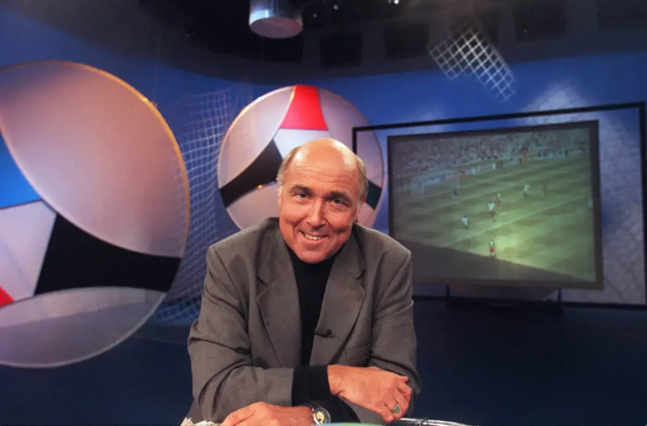 Ingvar Oldsberg ler i studion med fotbollsm&aring;l p&aring; sk&auml;rmen bakom.