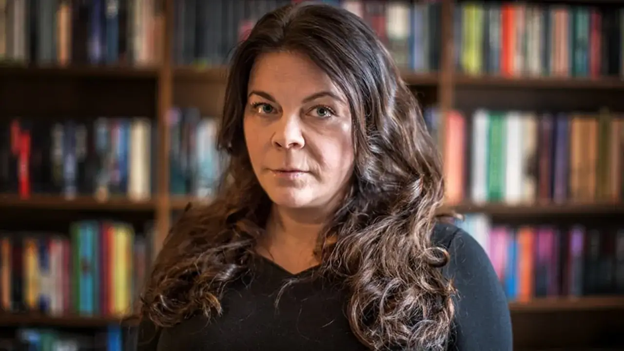Jennifer Wegerup, med sitt lockiga hår, sitter framför en bokhylla fylld med böcker.