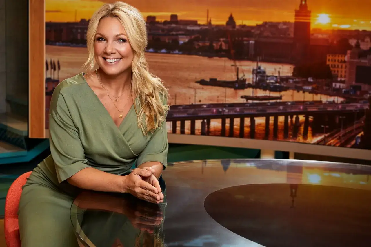Anna Brolin ler mot kameran i en grön klänning, med en bild av Stockholm i solnedgången bakom sig.