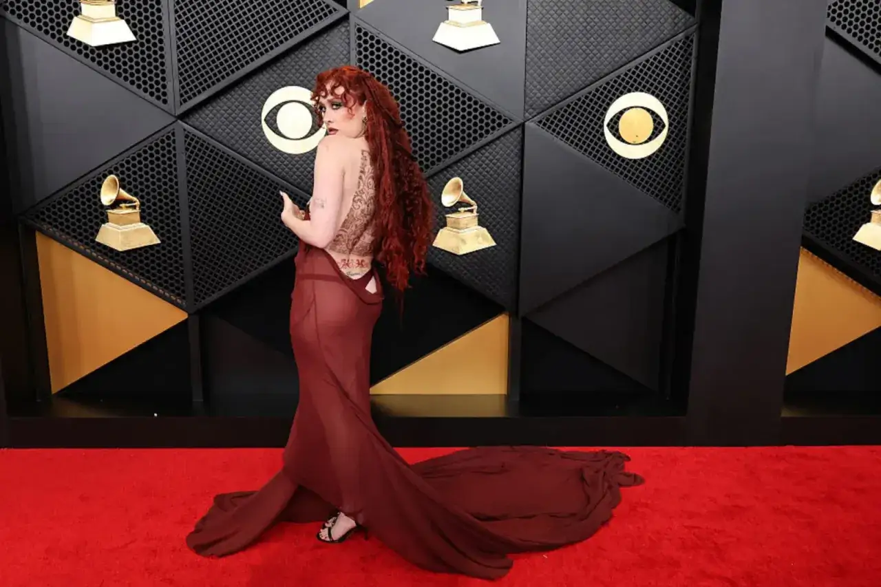 Chappell Roan i sin dramatiska Grammy-outfit, med en genomskinlig vinröd klänning och intrikat ryggtatuering, på röda mattan.