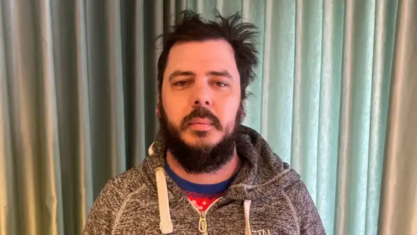 Man med rufsigt hår och skägg, klädd i en grå hoodie över en julig tröja. Han ser ut att ha haft en chang frick.