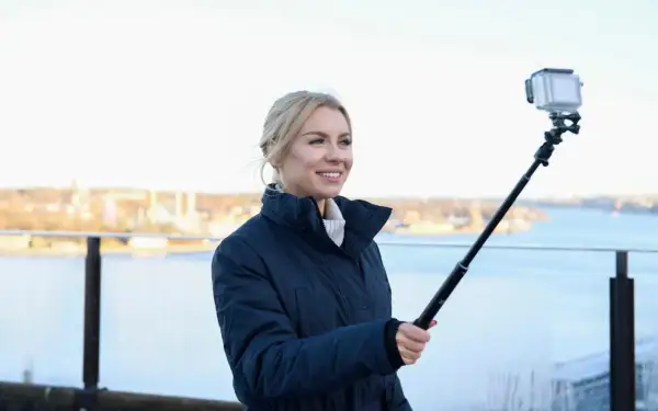 Therese Lindgren filmar med GoPro på selfiepinne vid en vattensamling med stad i bakgrunden.