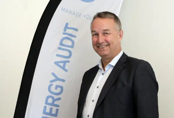 Thomas Ekman ler glatt framför en banderoll med texten "ENERGY AUDIT".
