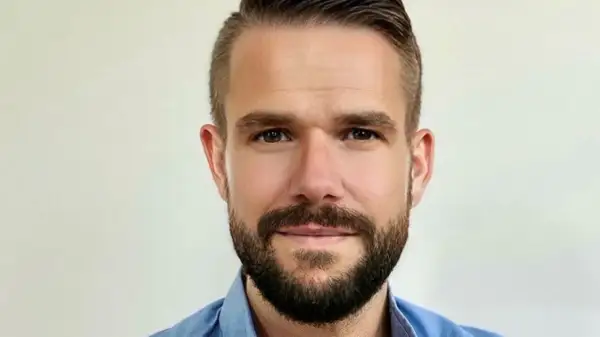 Johnny Kroneld, en man med kortklippt mörkt hår och skägg, bär en blå skjorta.