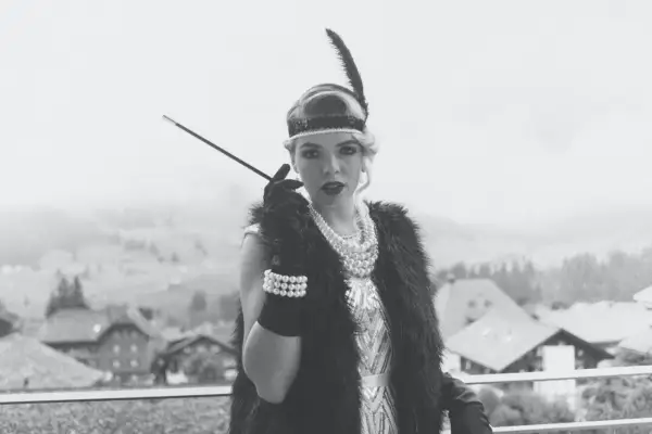 Kvinna i 1920-talsmode med fjäderpannband, pärlhalsband och cigaretthållare.