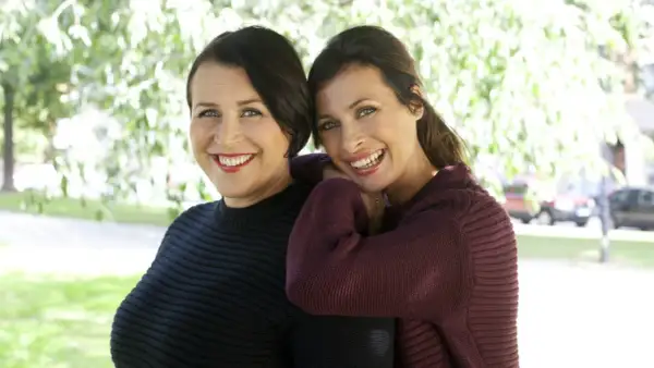 Två leende kvinnor, Hannah och Amanda, står nära varandra utomhus.