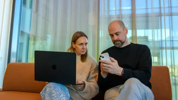 Man och kvinna sitter i soffa med laptop och mobil. De verkar diskutera något från samtiden tidning.