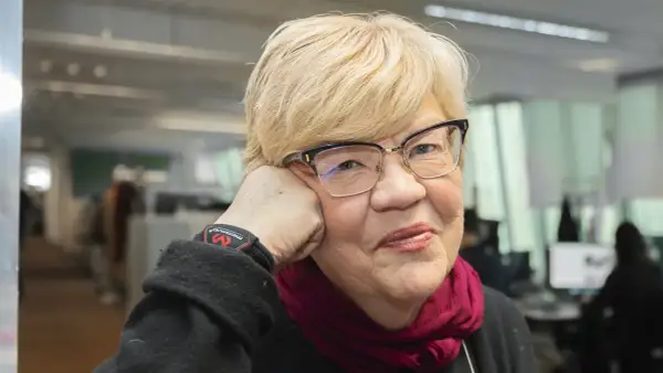 Lena Mellin med glasögon och en vinröd scarf vilar huvudet i handen.
