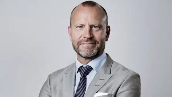 Peter Fellman, en man med gråsprängt skägg och blå ögon, bär en ljusgrå kavaj och randig slips.
